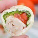 A close-up of a hand holding a turkey roll-up slice.