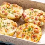 A dish with baked stuffed potatoes topped with cheese and bacon bits, garnished with chopped herbs.