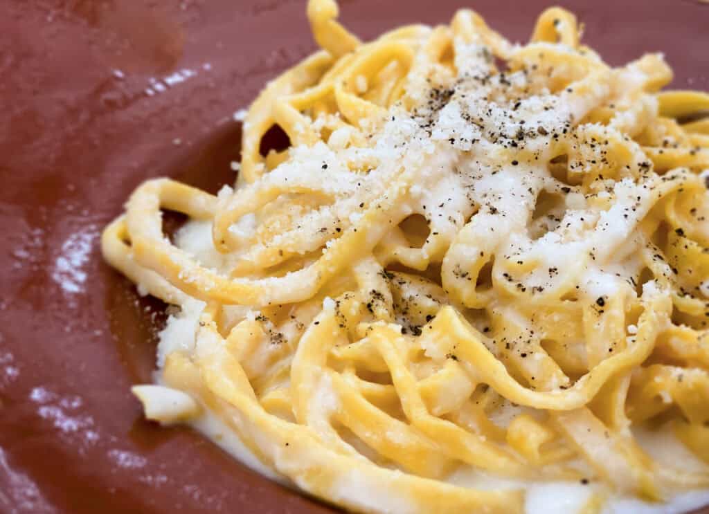 Close up of cacio e pepe on a brown plate. 