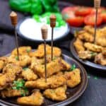 Plates of breaded and fried chicken nuggets with skewers, garnished with herbs.