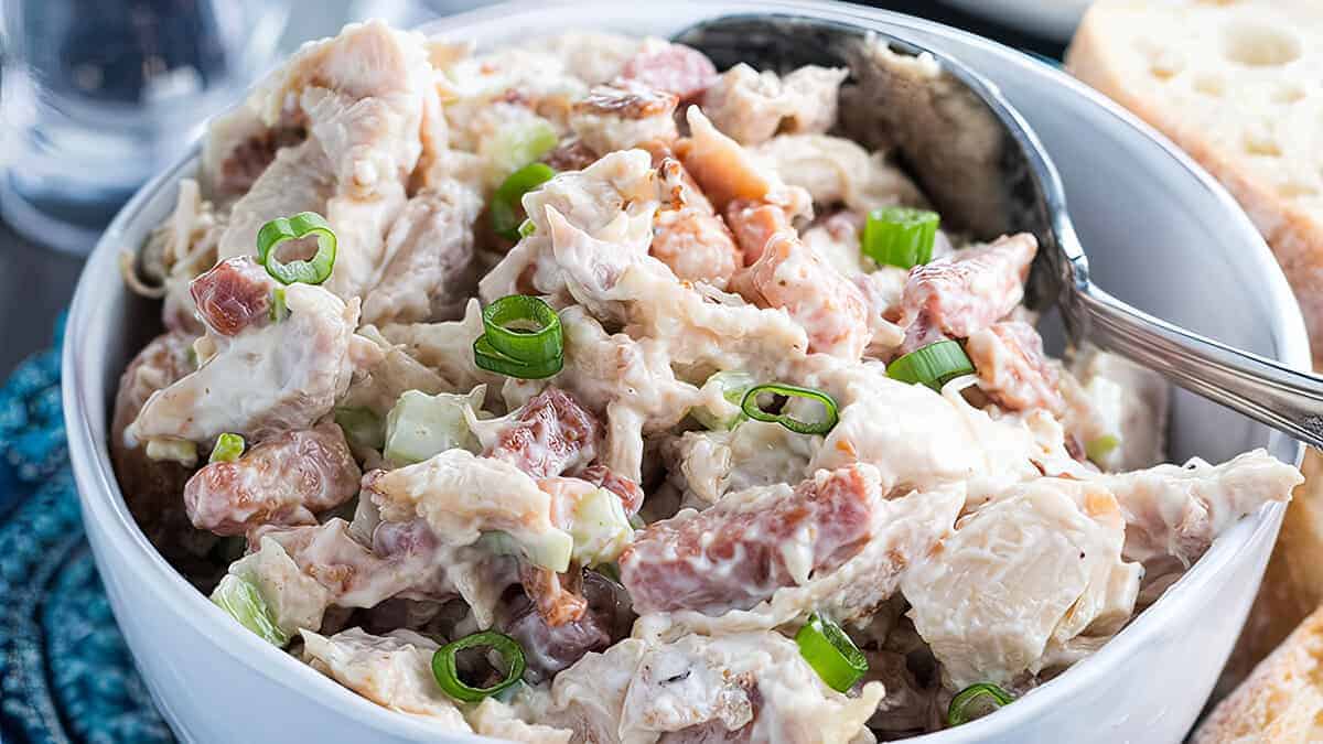 A bowl of chicken salad garnished with sliced green onions and sliced of bread next to it.