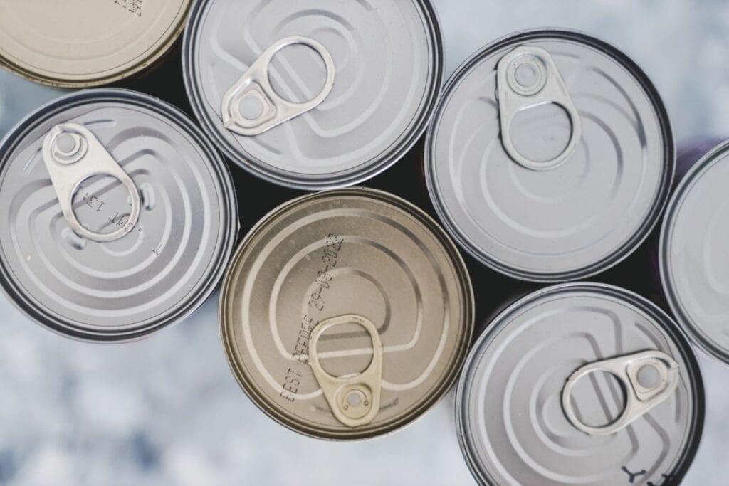 Top view of several metal food cans with pull tabs, one can is open, against a blurred background.