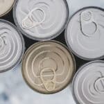 Top view of several metal food cans with pull tabs, one can is open, against a blurred background.