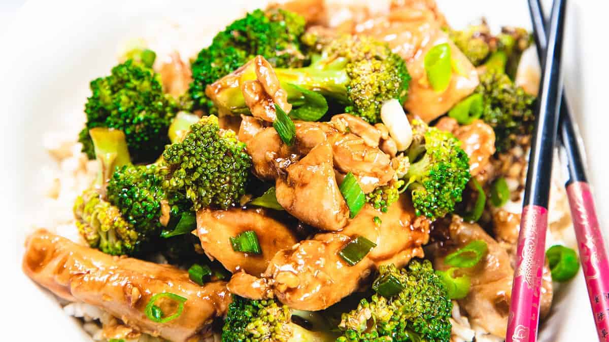 A chicken and Broccoli stir fry piled high on a white plate with chop sticks.