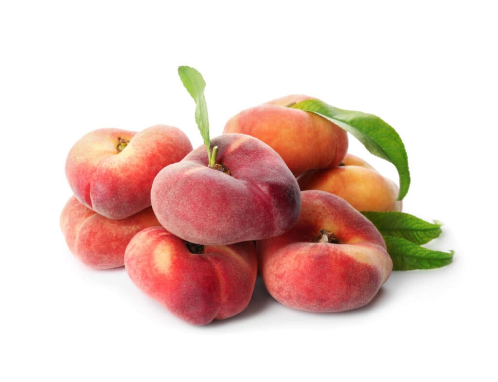 A pile of fresh, ripe flat peaches with leaves, isolated on a white background.