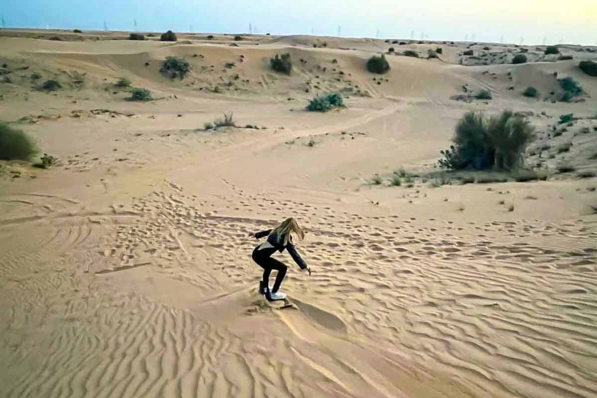 Sandboarding down a slope in Dubai desert.