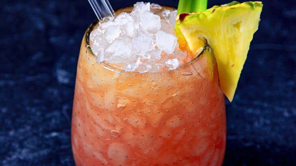 A close-up of a chilled, copper mug filled with iced cocktail, garnished with a pineapple slice and celery stalk.