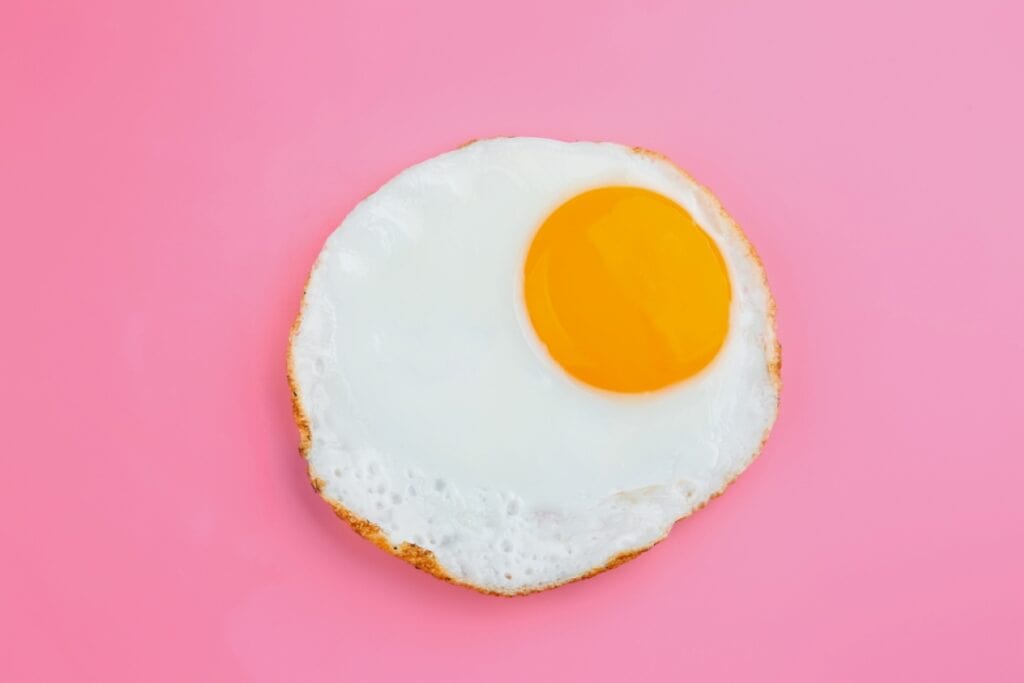 A single sunny-side-up egg with a bright yellow yolk on a pink background.