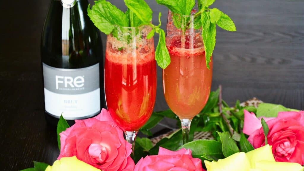 Two sparkling drinks garnished with mint, surrounded by pink and yellow roses, with a bottle of fre brut in the background.