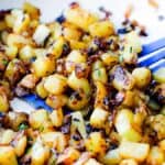 Fried Potatoes and Onion to a golden brown in a skillet, garnished with chopped herbs, with a blue spatula.