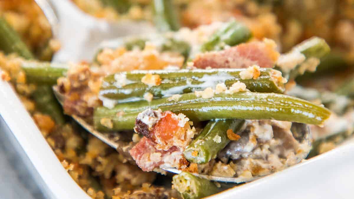 Green bean casserole with bacon being served with a spoon.