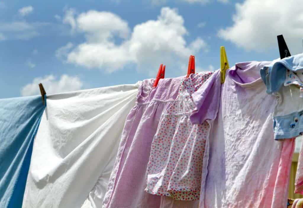 Clothes, including dresses and shirts, hanging on a clothesline with clothespins, drying under a partly cloudy sky.