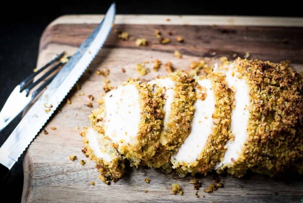 Sliced hazelnut crusted turkey breast on a wooden cutting board with a knife next to it.