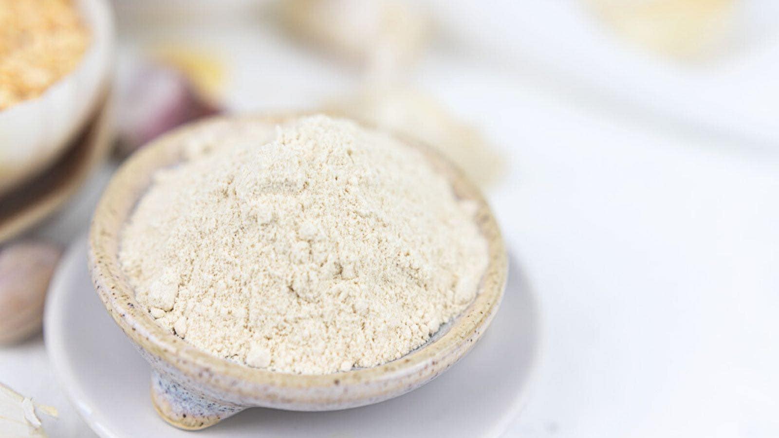 A bowl of fine garlic powder on a white surface.