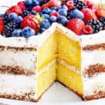 A layered lemon curd cake with a slice topped with assorted fresh berries like strawberries, blueberries, and blackberries on a white background.