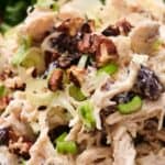 Close-up of a chicken salad topped with chopped pecans, green onions, and raisins, served on a bed of spinach leaves.