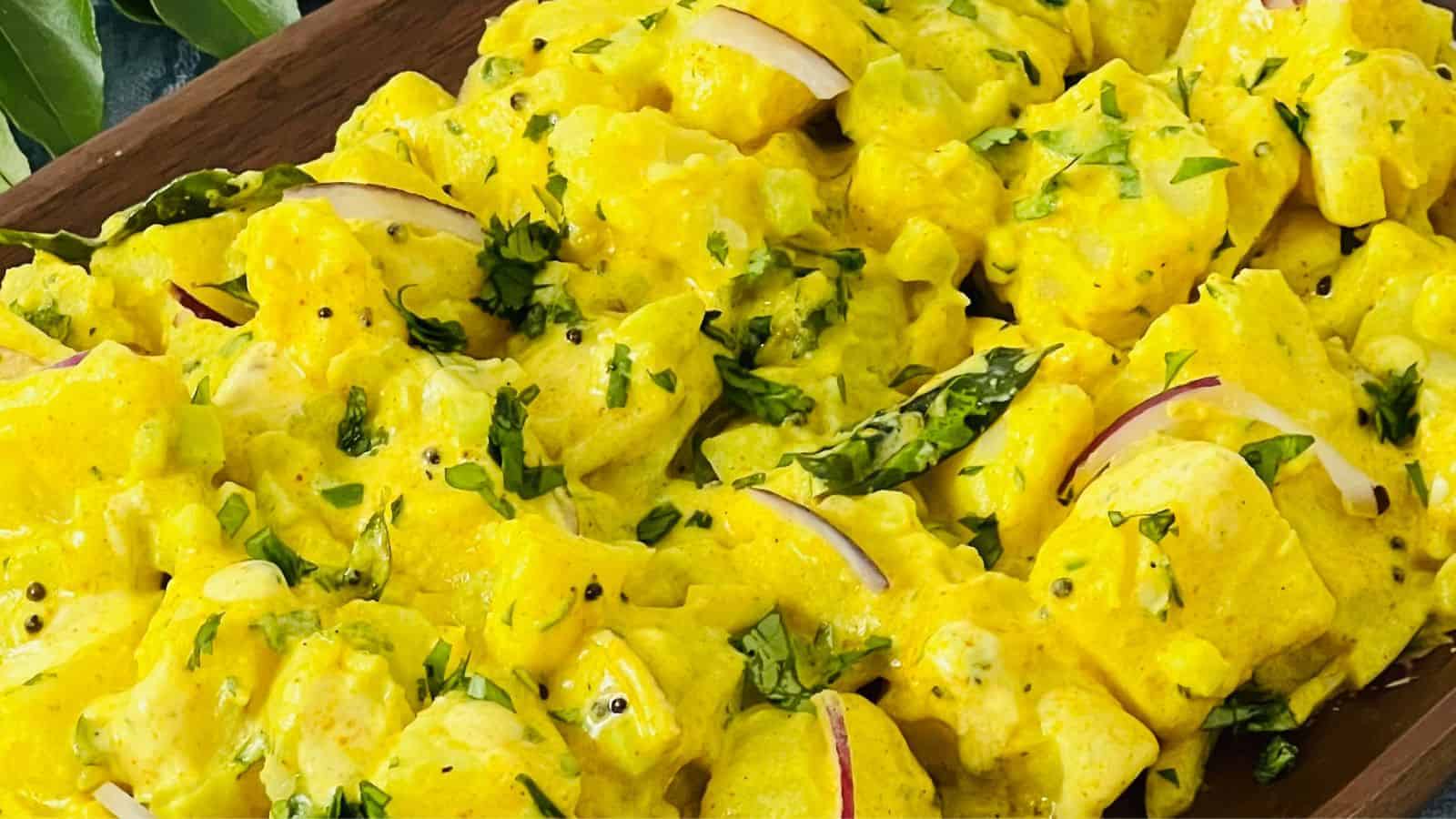 A dish of yellow curry with chunks of tofu, garnished with red onion slices, chopped greens, and green chili peppers.