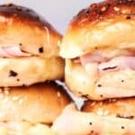 Four ham and cheese sliders on brioche buns are stacked, showcasing their melted cheese and sesame seed toppings.