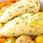 A dish of seasoned chicken breasts garnished with parsley, surrounded by carrots and potatoes in a bowl.