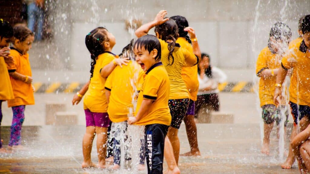 Children in yellow shirts playing joyfully in water fountains.