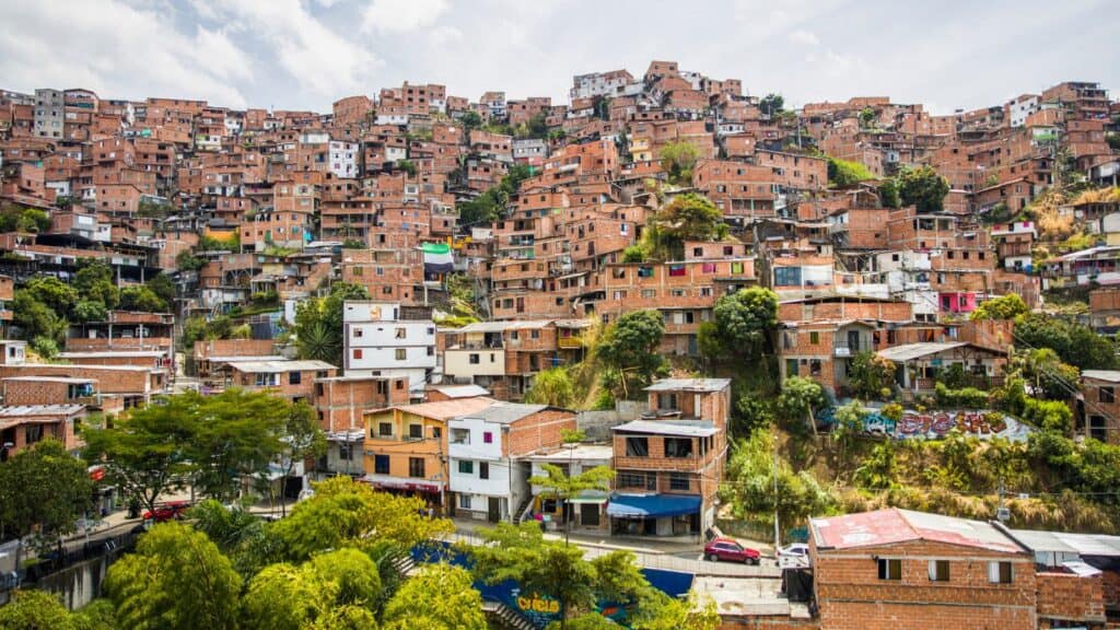 Densely packed colorful houses on a hillside in a sprawling urban slum under a bright sky.