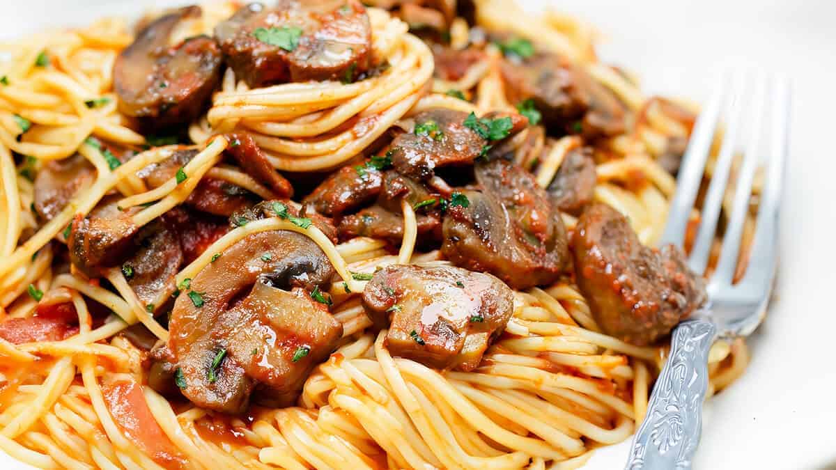 A close up image of plate with a serving of spaghetti topped with a tomato mushroom sauce.