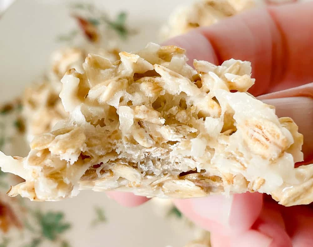 Close-up of a hand holding a piece of oat and coconut granola bar, showing its chewy texture.