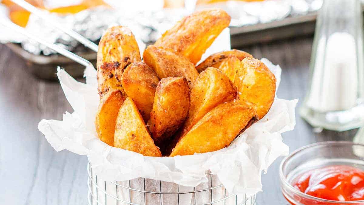 Seasoned Baked Potato Wedges in a metal serving basket sprinkled with salt.