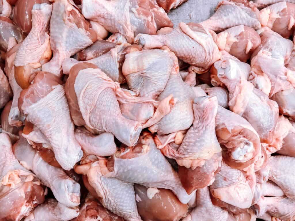 A pile of raw chicken drumsticks and thighs displayed on a table.