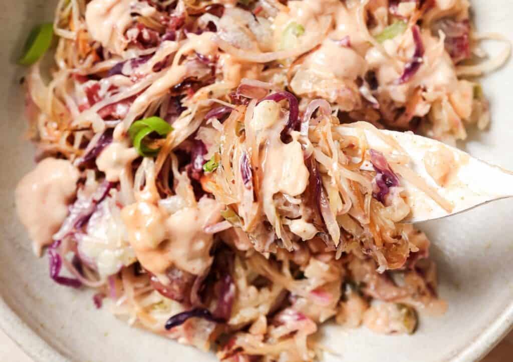 A bowl of creamy coleslaw with red and white cabbage, topped with green herbs, served with a fork.