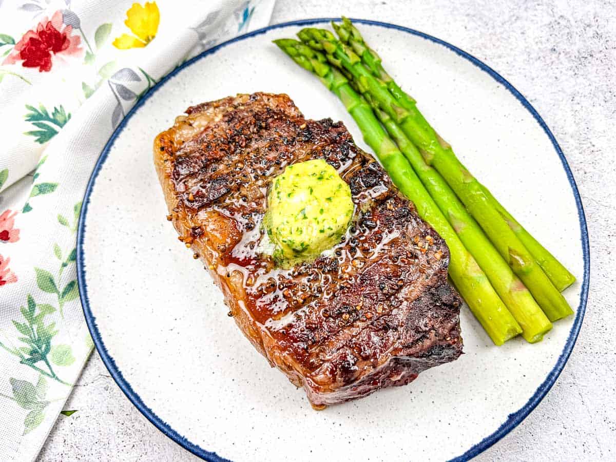 Reverse Seared Smoked Steaks with Smoked Garlic Butter on a plate with asparagus.