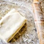 A piece of rough puff pastry dough and a rolling pin on a table.