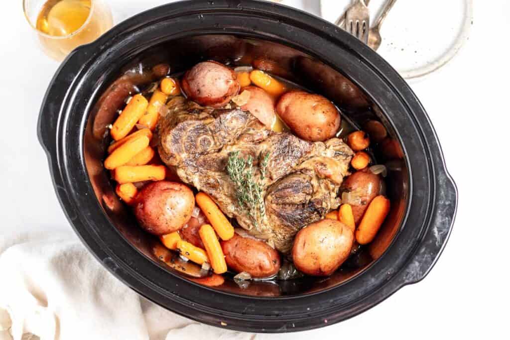 A slow cooker filled with a hearty meal of pot roast, carrots, and potatoes, viewed from above.
