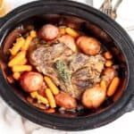 A slow cooker filled with a hearty meal of pot roast, carrots, and potatoes, viewed from above.