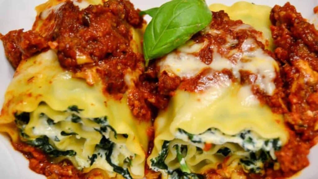 Two stuffed manicotti pasta shells with ricotta and spinach filling, topped with marinara sauce and melted cheese, garnished with a basil leaf.
