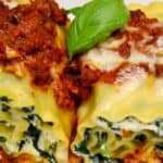 Two stuffed manicotti pasta shells with ricotta and spinach filling, topped with marinara sauce and melted cheese, garnished with a basil leaf.