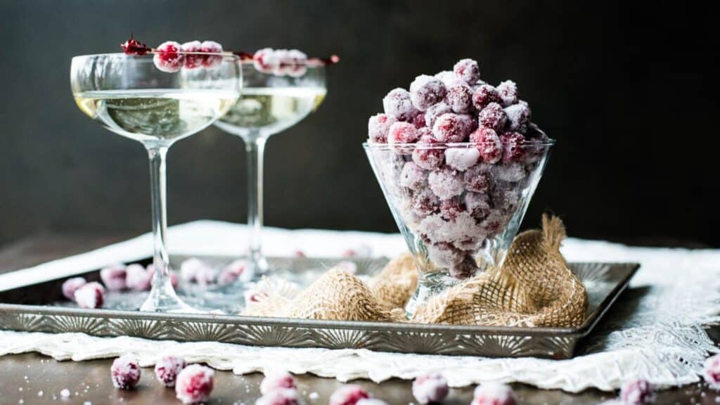 Sugared cranberries in a stemless martini glass next to two glasses of champagne.