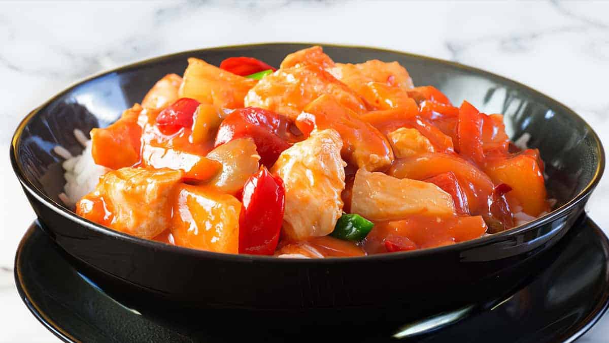 A close up image of a bowl full of Sweet and sour chicken over rice.