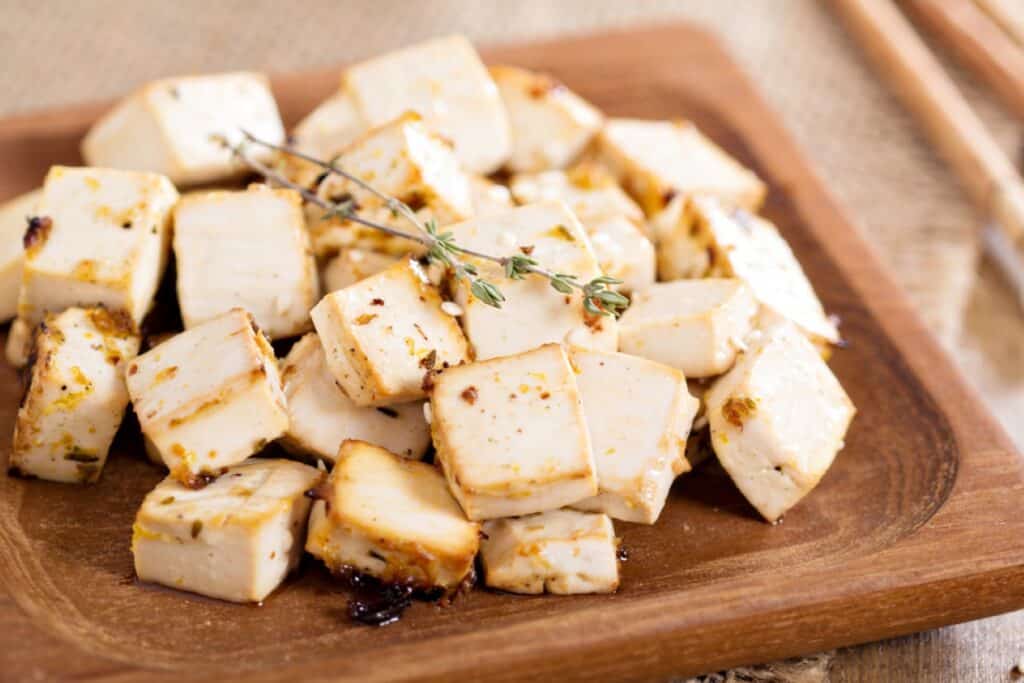 Cubed tofu pieces seasoned with herbs on a wooden plate.