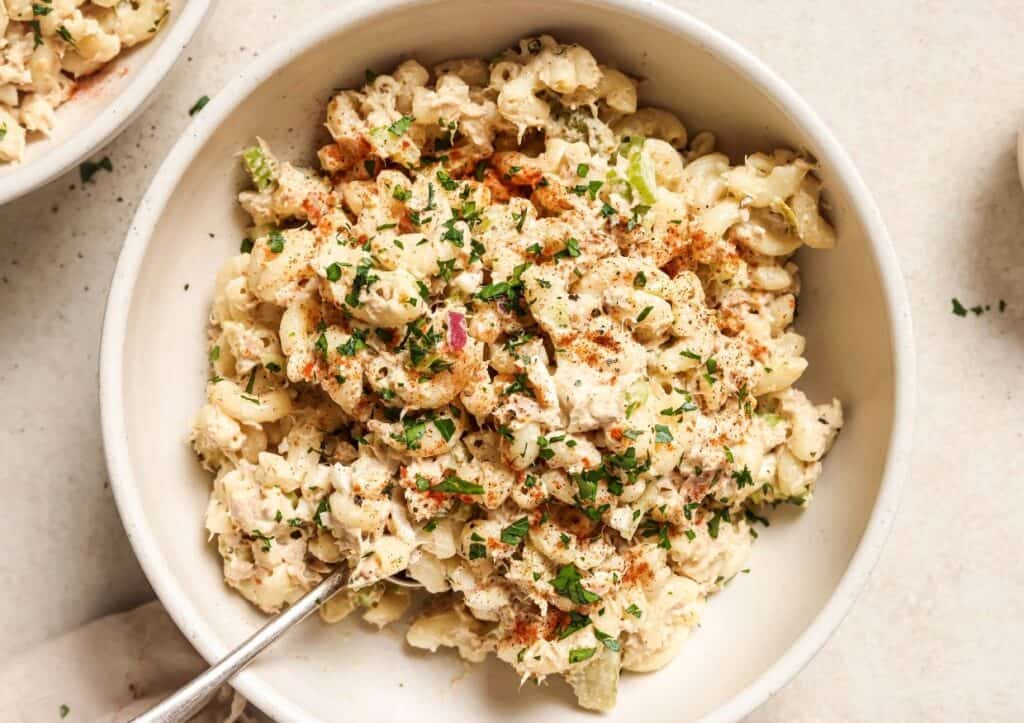 A bowl of creamy macaroni salad garnished with herbs and sprinkled with paprika.