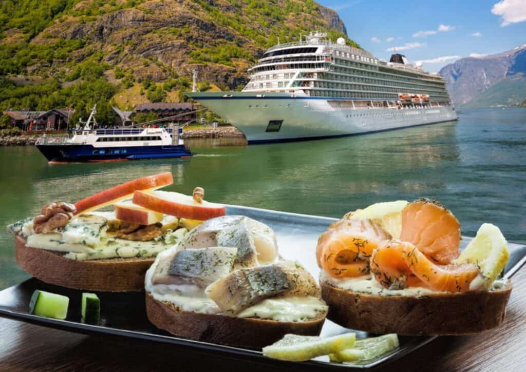 A cruise ship docked at a scenic mountain lake with a close-up of sandwiches with various toppings in the foreground, highlighting one of the best foodie destinations.