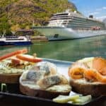 A cruise ship docked at a scenic mountain lake with a close-up of sandwiches with various toppings in the foreground, highlighting one of the best foodie destinations.