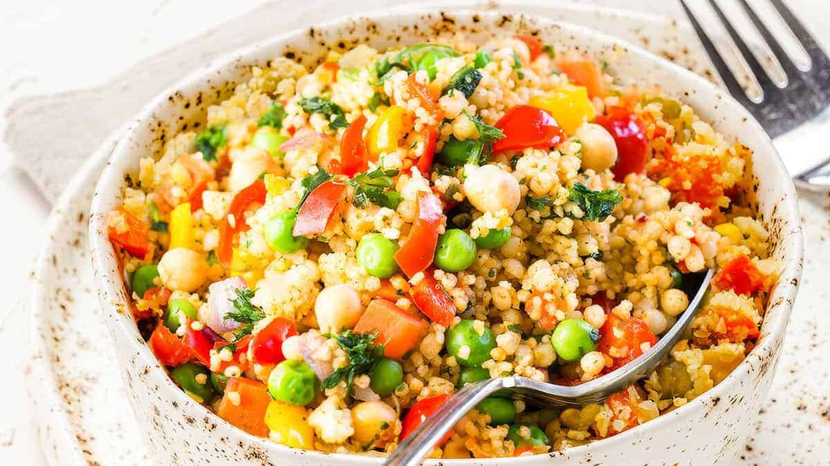 A close up image of Vegetable Moroccan Couscous in a bowl with a serving spoon.