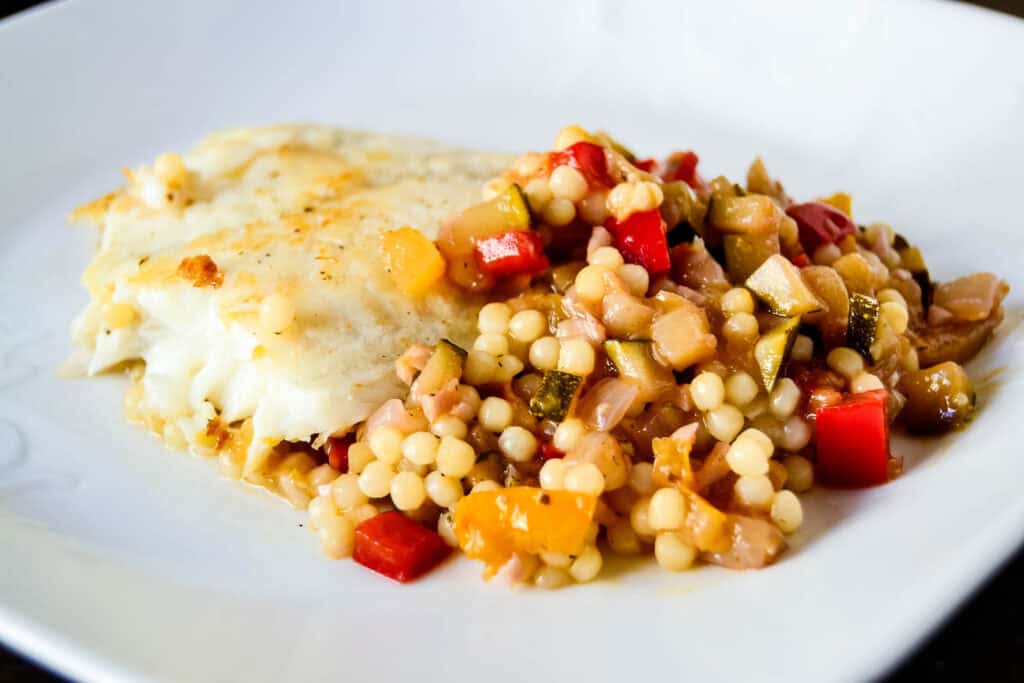 Sauteed fish fillet served with a side of mixed vegetables and couscous on a white plate.