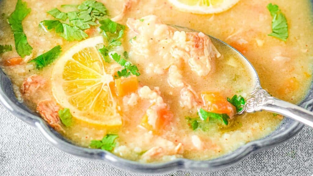 A bowl of lemon and shrimp soup garnished with parsley, with a spoon on the side.