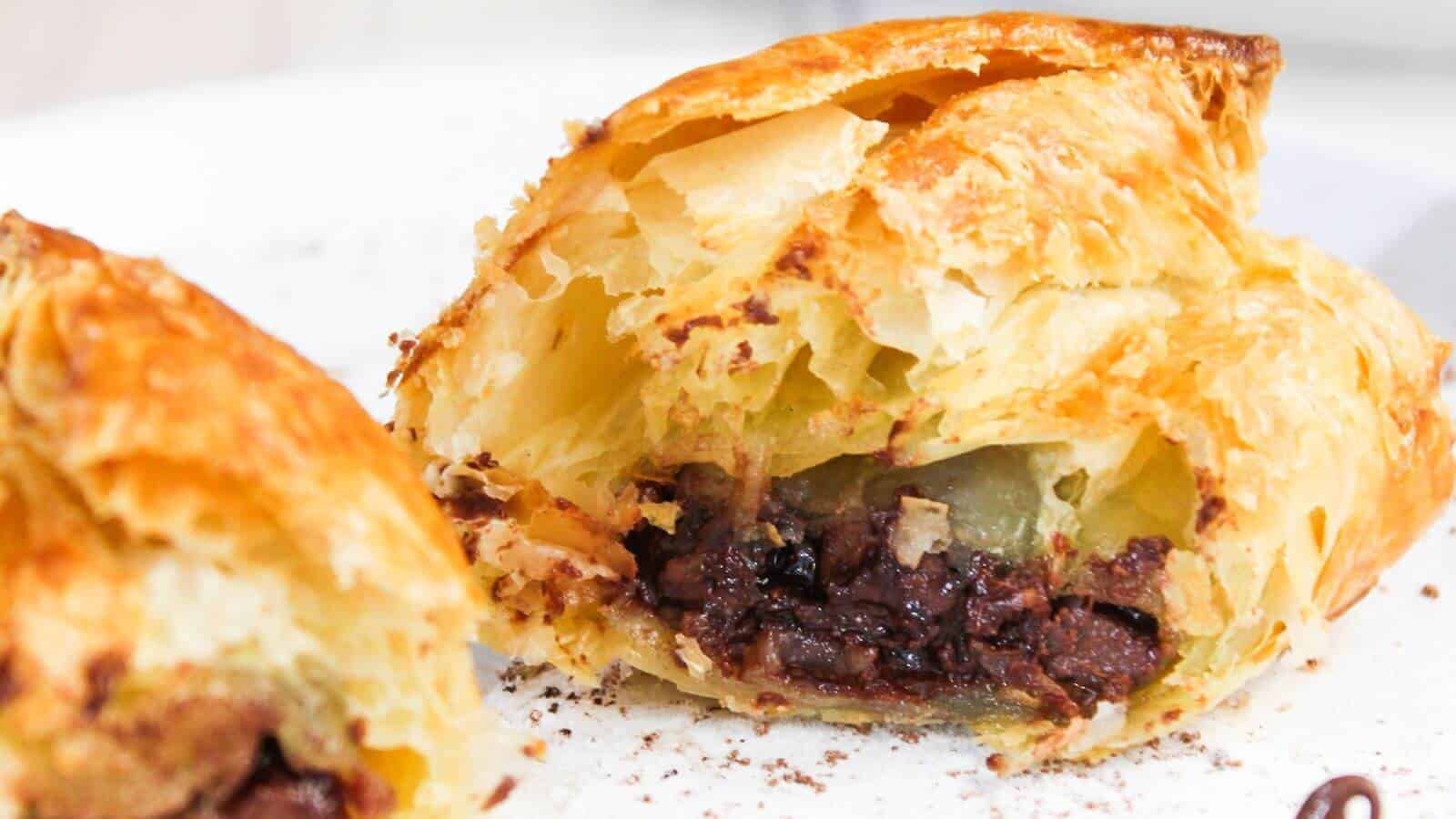Close-up of a flaky pastry cut open to reveal a filling of chocolate, with a visible crispy golden crust.