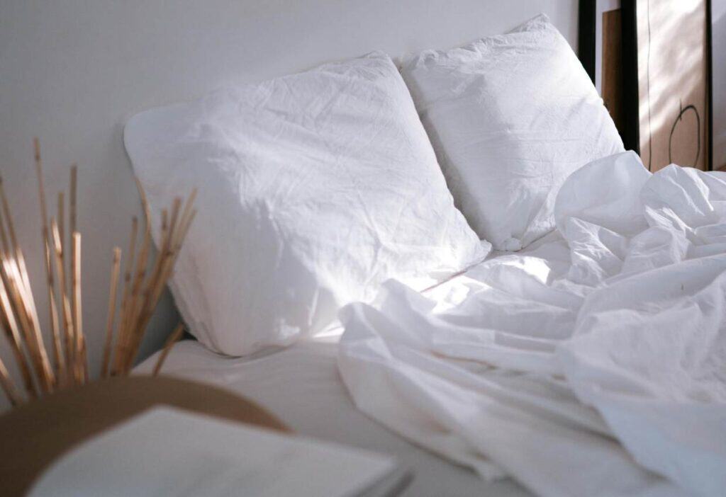 A bed with white linens, lit by the sun.