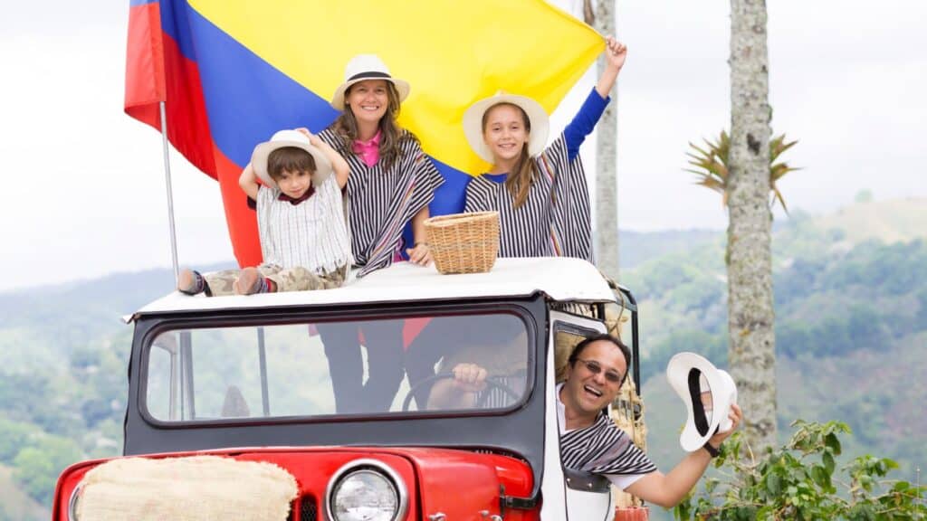 A happy family of four, dressed in striped tops, enjoying a picnic on top of a red vintage car under the colombian flag in a scenic landscape.