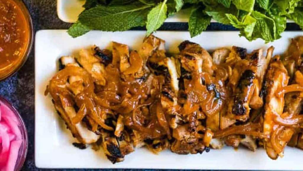 Grilled chicken topped with caramelized onions and served with fresh herbs on a white rectangular plate.