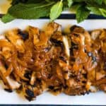 Grilled chicken topped with caramelized onions and served with fresh herbs on a white rectangular plate.